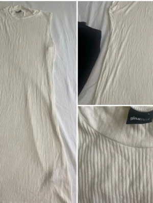 Vit ribbad klänning Gina Tricot - Snygg vit ribbad klänning från Gina Tricot med hög hals och ärmlös design. Klänningen har en rak passform och är tillverkad i ett mjukt, stretchigt material som sitter bekvämt. Perfekt för en stilren look.