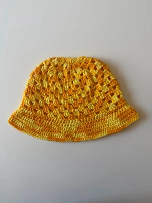 Gul virkad bucket hat - Handgjord bucket hat i virkad bomull, i underbar gul. Hatten har ett luftigt mönster och brett brätte, perfekta för en trendig och avslappnad stil. Säljs styckvis. 