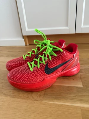 Reverse grinch sneakers  - Nike sneakers i storlek 41 rött med texturerad ovandel och svart swoosh på sidan. Skorna har iögonfallande neongröna snören och en låg siluett. Yttersulan är också röd med detaljer i svart och grönt. Perfekt för dig som vill sticka ut med färg och stil.