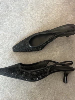 Svarta glittriga sandaler/pumps - Säljer ett par svarta pumps med spetsig tå och låg klack. Mycket god skick, använda endast 1 gång på en fest. Är som helt nya!