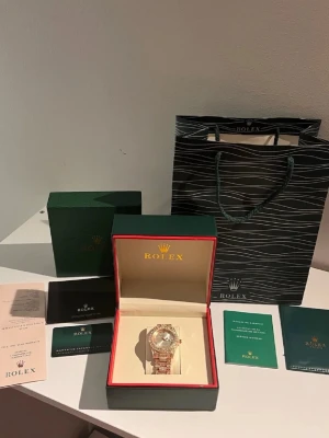 Klocka  - Exklusiv lyxklocka med helisad design och gnistrande stenar över boett, länk och vridring. Klockan har en elegant roséguldsfärgad finish, silverfärgad urtavla med datumvisning samt automatisk urverkskänsla. Levereras komplett med box, certifikat, manualer, kort och tillbehör precis som på bilderna. En iögonfallande modell som passar både till vardag och fest.