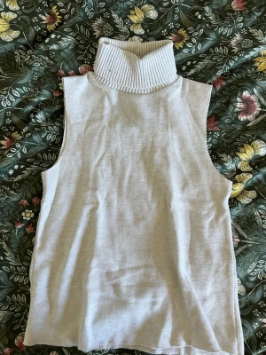 Beige ribbad polotopp från Zara - Säljer en beige ribbad polotopp från Zara. Toppen är ärmlös med hög, bred polokrage och har en mjuk, stretchig känsla. Perfekt fest topp eller när man vill klä upp sig lite☺️☺️ Använd 1 gång!