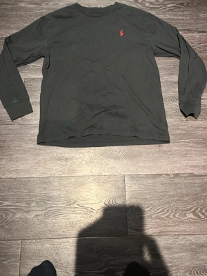 Svart långärmad tröja från Polo Ralph Lauren - Svart långärmad tröja från Polo Ralph Lauren med den klassiska röda logotypen broderad på bröstet. Tröjan har rund halsringning och är tillverkad i mjukt bomullsmaterial. Perfekt för en clean och stilren look.