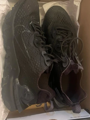 Svarta Nike sneakers med snörning - Säljer ett par svarta Nike sneakers med perforerat mesh-tyg och robust sula. Skorna har klassisk snörning och diskret swoosh på sidan. Perfekta för dig som gillar sportig och stilren look.