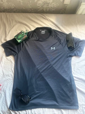 Svart tränings-tshirt från Under Armour - Säljer en svart funktions-tshirt från Under Armour med klassisk logga på bröstet. T-shirten har rund hals och korta ärmar, tillverkade i ett lätt och snabbtorkande material som passar perfekt till träning och sport.Pris kan diskuteras.