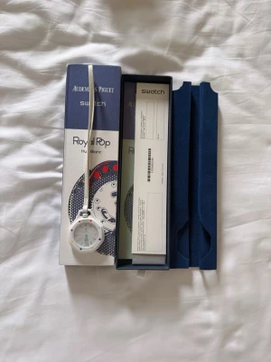 Vit Royal Pop klocka Swatch x Audemars Piguet - Säljer en Royal Pop klocka från Swatch x Audemars Piguet i modellen Huit Blanc. Klockan har en vit rem och boett, rund urtavla med färgglada detaljer och minimalistisk design. Kommer i originalförpackning med tillhörande box och papper.