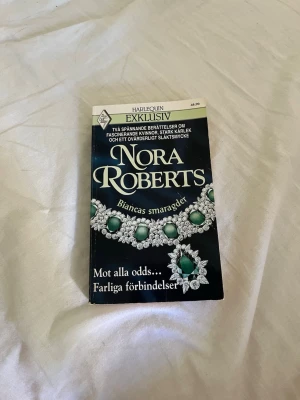 Biancas smaragder av Nora Roberts - En spännande pocketbok från Nora Roberts, 'Biancas smaragder', med ett elegant omslag i mörkblått och grönt smyckesmotiv. Boken innehåller två berättelser om kärlek, farliga förbindelser och familjehemligheter. Perfekt för dig som gillar romantik och drama.