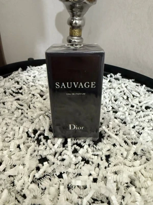 Dior Sauvage Eau de Parfum - Dior Sauvage Eau de Parfum i en elegant, mörkblå rektangulär glasflaska med silverdetaljer och tydlig logga på toppen. Flaskan har en stilren och lyxig design som verkligen sticker ut på parfymhyllan. Perfekt för dig som gillar exklusiva dofter. Helt ny 