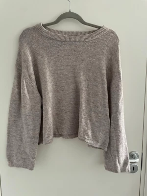 Beige oversized stickad tröja - Mysig beige stickad tröja med avslappnad, oversized passform och bred halsringning. Tröjan har långa ärmar och ribbade muddar vid hals, ärmslut och nederkant. Perfekt för lager på lager och chill dagar.