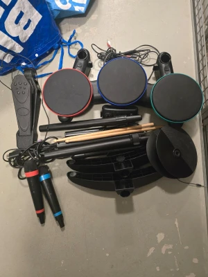 Trumset till spelkonsol med mikrofoner - Säljer ett komplett trumset till spelkonsol med tre färgmarkerade trumplattor, pedal, två mikrofoner och trumpinnar. Trumplattorna har röda, blå och gröna kanter. Allt är i svart plast och passar perfekt till musikspel som Rock Band eller Guitar Hero. Trumset är till Xbox 360 det bara ligger i förrådet säljer i befintlig skick 