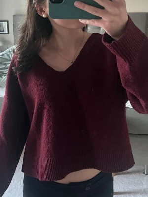 Vinröd stickad V-ringad tröja - Mysig vinröd stickad tröja med V-ringning och långa ärmar från BikBok. Tröjan har en avslappnad passform och ribbstickade muddar vid ärmslut och nederkant.