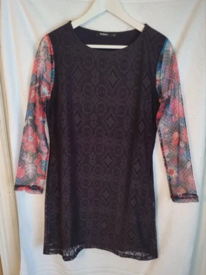 Klänning - Svart klänning från Desigual i storlek 40. Ärmarna är gjorda av ett genomskinligt tyg med blommönster. Det finns en dragkedja på sidan av klänningen. Mycket fint skick och normal i storleken.