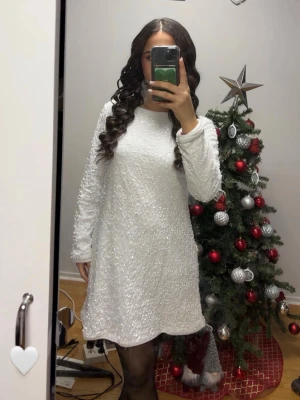 Vit paljettklänning med lång ärm - Säljer en vit kortklänning med långa ärmar och täckt av glittriga paljetter. Klänningen har en rak passform och rund halsringning, perfekt för dig som vill sticka ut. Materialet känns festligt och skimrande.