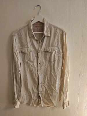 Beige långärmad skjorta med fickor - Stilren beige skjorta från Camel Active med långa ärmar och två bröstfickor med lock. Skjortan har klassisk krage och knappar framtill. Perfekt för en avslappnad men snygg look.