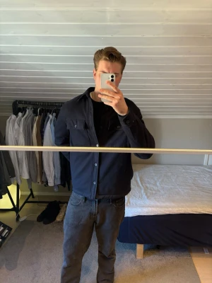 Marinblå overshirt med fickor - Stilren svart overshirt med knäppning framtill och två bröstfickor med lock. Klassisk krage och raka linjer ger en clean look. Perfekt att bära öppen eller stängd över t-shirt. Materialet ser ut att vara bomull eller en bomullsblandning. 