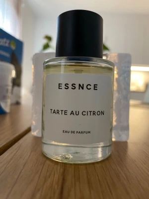 ESSNCE Tarte Au Citron Eau de Parfum - Fräsch parfym från ESSNCE med doft av citronpaj. Flaskan är genomskinlig med en enkel vit etikett och svart text, samt ett stilrent svart lock. Perfekt för dig som gillar fräscha och söta citrusdofter.