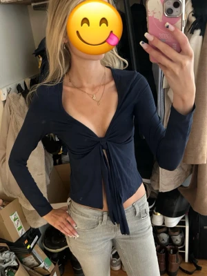 Mörkblå långärmad knytblus - Trendig mörkblå topp med långa ärmar och djup urringning. Toppen har en snygg knytning framtill som ger en cool och avslappnad look. Perfekt att styla med jeans eller kjol för en modern outfit. Inga lappar finns. Skriv för exakta mått. Är 170cm och har S/XS i storlek. 