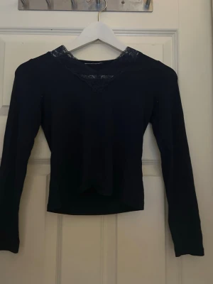 Svart långärmad topp med spets - Snygg svart långärmad topp med v-ringning och dekorativ spetsdetalj vid halsen. 