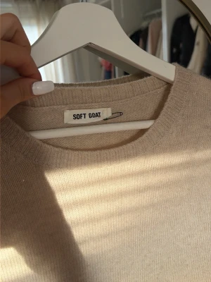 Beige stickad t-shirt från Soft Goat - Beige stickad t-shirt från Soft Goat i mjuk och lyxig kvalitet. Tröjan har korta ärmar, rund halsringning och ribbstickade kanter. Perfekt för en stilren och avslappnad look. 100% cashmire 