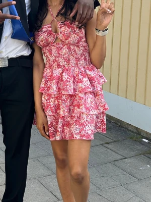 Blommig rosa volangklänning - Supersöt kort klänning med rosa och vita blommor, volanger och smock i midjan. Sommar klänning