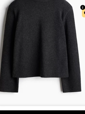Mörkgrå stickad tröja med rund hals - En stilren mörkgrå stickad tröja med rund hals och långa ärmar. Tröjan har bred ribbstickad kant nedtill och vid ärmsluten, vilket ger en snygg och modern siluett. Perfekt för lager på lager och enkel att matcha med olika outfits.