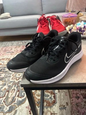 Svarta Nike sneakers med vit sula - Snygga svarta Nike sneakers med vit sula och klassisk vit swoosh på sidan. Skorna har lågt skaft och ovandel i mesh för bra andningsförmåga. Perfekta för dig som vill ha en clean och sportig look till vardags.