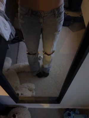 Ljusblå ripped jeans med raka ben - Säljer ett par ljusblå jeans med raka ben och slitningar över knäna. Jeansen har klassisk femficksmodell och låg midja. Perfekta för en avslappnad och trendig look. Materialet är denim i bomull. Passar dig som gillar streetstyle och casual vibes.