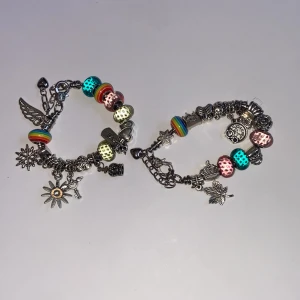Två färgglada berlockarmband - Två armband med silverfärgade länkar och massor av detaljerade berlocker, bland annat fjäril, blomma, stjärna och hjärta. Armbanden har pärlor i regnbågsfärger, turkost, rosa och grönt samt flera metallberlocker med olika former. Perfekt för dig som gillar unika accessoarer. Jag gjorde de själva. Kan byggas om om man vill. 😻😻😻. Kan köpas tillsammans eller styck.