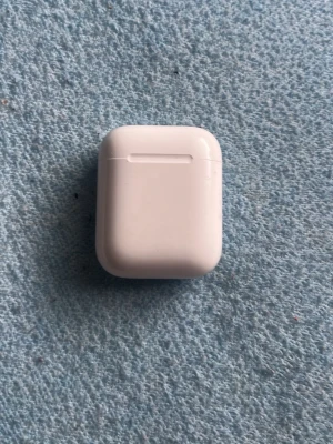 Trådlösa vita hörlurar Apple AirPods - Säljer ett par stilrena vita Apple AirPods med laddningsetui. Hörlurarna är trådlösa och har en smidig, kompakt design i blank plast. Perfekta för musik, poddar och samtal på språng. Laddningsetuiet har magnetlock och LED-indikator.