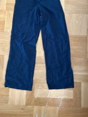 Mörkblå vida linnebyxor - Säljer ett par mörkblå linnebyxor med avslappnad passform och raka ben. Byxorna har dragsko i midjan för extra komfort och är tillverkade i ett lätt och luftigt linnematerial. 