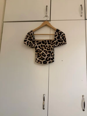 Leopardmönstrad topp med puffärm - Trendig topp med leopardmönster och fyrkantig urringning. Modellen har korta puffärmar och croppad passform. Perfekt för dig som vill sticka ut med en djurisk look.