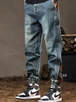 Baggy jeans med bruna detaljer - Säljer ett par baggy jeans i ljusblå denim med bruna paneler längs sidorna och elastiska muddar vid bensluten. Jeansen har knappar längs benen och en avslappnad passform som ger en streetwear-vibe. Perfekta för dig som gillar en unik och trendig stil.