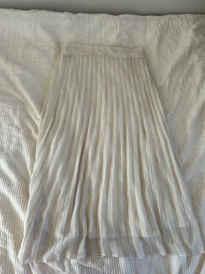 Plisserad beige långkjol - Säljer en elegant plisserad långkjol i ljusbeige ton. Kjolen har ett mjukt, flytande tyg och resår i midjan för skön passform. Perfekt för dig som gillar stilrena och klassiska plagg. Superfin på sommar och vår!💗