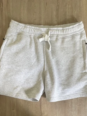 Russemerch shorts gråa - Snygga ljusgrå mjukisshorts med snörning i midjan och två sidofickor. Perfekta för chill dagar eller träning. Tillverkade i mjukt bomullsmaterial för maximal komfort och avslappnad stil.