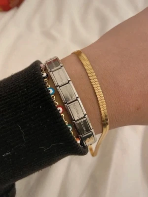 Armband - Säljer ett coolt armband i silverfärgat rostfritt stål. Armbandet består av flera rektangulära länkar som kan byggas om och anpassas med olika charms. Perfekt för dig som gillar att skapa din egen stil och vill ha ett personligt smycke.
