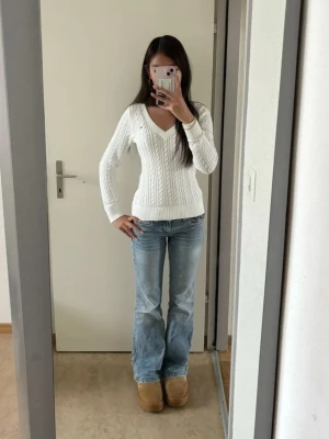 Vit kabelstickad tröja med v-ringning - Säljer en vit kabelstickad tröja med v-ringning och långa ärmar. Tröjan har ribbade muddar vid ärmslut och nederkant, samt ett klassiskt stickat mönster. Perfekt för dig som gillar en clean och stilren look.