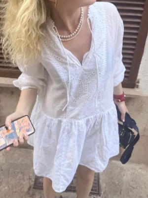 Vit klänning med broderi - Säljer en luftig vit klänning med broderade detaljer framtill och v-ringning med knytband. Klänningen har trekvartsärmar och volangkjol. Storlek S men passar M. Köpt på plick men är ifrån Hm!!💓💓💓