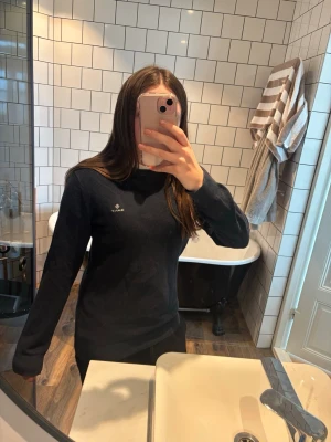 Mörkblå tröja från GANT - Snygg mörkblå stickad tröja från GANT med  logga på bröstet. Tröjan har rund halsringning och ribbade muddar vid ärmslut och nederkant. Perfekt till jeans eller kjol för en clean och klassisk look. Passar både tjejer och killar. 