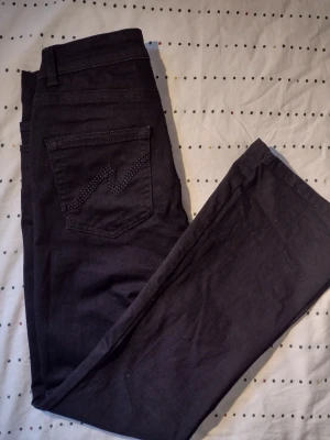 Svarta jeans från Nelly med detaljer - Snygga svarta jeans från Nelly med klassisk femficksdesign och dekorativa nitar på bakfickan. Jeansen är av ett stretchigt matrial och har en low cut. Storlek 38/short. Perfekta för dig som vill ha en stilren och trendig look.