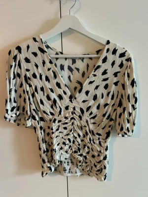 Mönstrad omlottopp med rynkdetaljer - Säljer en beige och svart omlottopp med v-ringning och rynkade detaljer framtill. Toppen har korta puffärmar och ett leopardinspirerat mönster. 