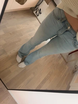 Ljusblå bootcut jeans - Säljer ett par ljusblå bootcut jeans med klassisk femficksmodell och normal midja. Jeansen har en snygg tvättad look och är tillverkade i ett mjukt denimtyg med lite stretch för extra komfort. Perfekta för en avslappnad och trendig stil.