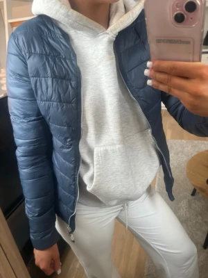 Mörkblå pufferjacka med dragkedja - Snygg mörkblå pufferjacka med quiltad design och smal passform. Jackan har dragkedja framtill och står upp lite i kragen. Perfekt för kalla dagar och enkel att matcha med olika outfits.