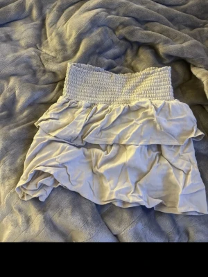 Beige volangkjol med smock - Supersöt beige kortkjol från lager 157 med bred smock i midjan och dubbla volanger. Kjolen har en luftig och flowy känsla, perfekt för varma dagar. Passar dig som gillar en feminin och trendig stil. Storlek 140. Men passar mig som har xxs