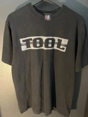 Svart TOOL t-shirt med tryck - Cool svart t-shirt från Gildan med stort vitt TOOL-tryck på bröstet. Klassisk passform med rund hals och korta ärmar. Perfekt för dig som gillar bandmerch och vill ha en enkel men snygg look.