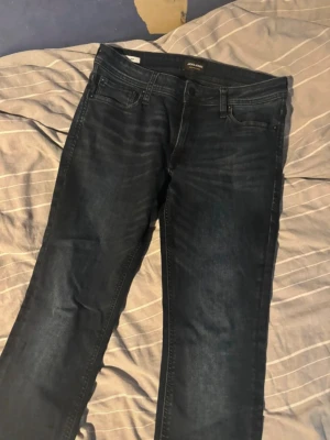 Mörkblå jeans från Jack & Jones - Snygga mörkblå jeans från Jack & Jones med klassisk femficksmodell och diskreta slitningar. Jeansen har normal midja, bälteshällor och knappgylf. Perfekta för dig som gillar en stilren och enkel look.