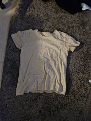 Beige basic t-shirt i bomull - En enkel beige t-shirt i mjuk bomull med rund hals och korta ärmar. Perfekt till vardags och lätt att matcha med olika stilar. Klassisk passform och utan tryck eller mönster.