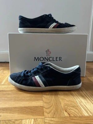 Moncler mörkblåa sneakers i mocka - Snygga mörkablåa sneakers från Moncler i  mocka med den klassiska Moncler loggan vid sidorna. låg modell med vita sulor. Perfekta skor för när det blir varmare! Säljer skorna nu för 1199kr! Skriv om du har några funderingar.