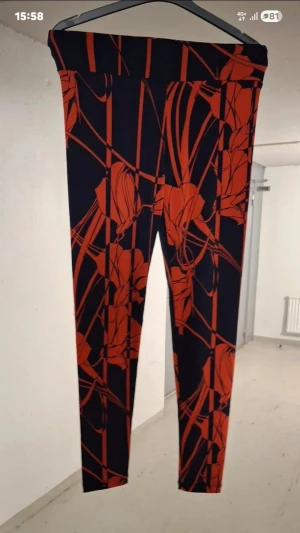Svarta mjukisbyxor med rött mönster - Säljer ett par svarta mjukisbyxor med stora röda blommönster och grafiska linjer. Byxorna har hög midja och smal passform, perfekta för en trendig och avslappnad stil. Materialet känns mjukt och stretchigt, vilket gör dem riktigt bekväma.