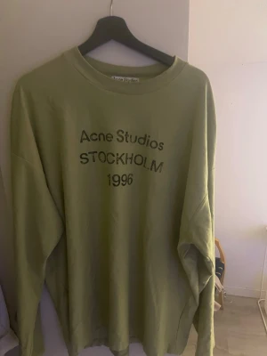 Grön longsleeve  Acne Studios T-shirt  - Grön longsleeve från Acne Studios med tryck 'STOCKHOLM 1996' på bröstet. Tröjan har rund halsringning och avslappnad passform, perfekt för en stilren och trendig look. XL men passar bättre L