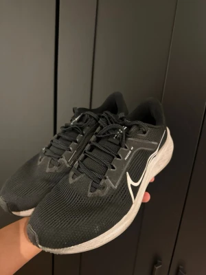 Nike Pegasus 40 - Snygga svarta Nike löparskor med vit sula och diskreta grå detaljer. Skorna har en mesh-överdel för bra ventilation och klassisk snörning. Perfekta för dig som gillar sportig stil och vill ha bekväma skor till vardags.